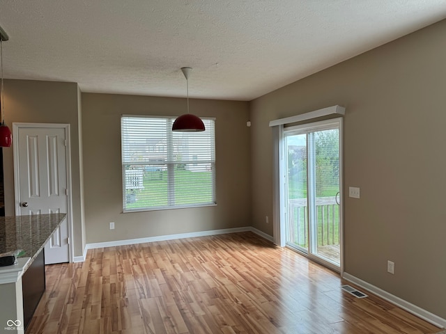 unfurnished dining area with a textured ceiling and light hardwood / wood-style flooring