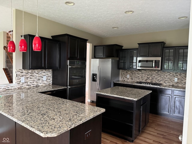 kitchen with decorative backsplash, stainless steel appliances, a center island, decorative light fixtures, and hardwood / wood-style floors