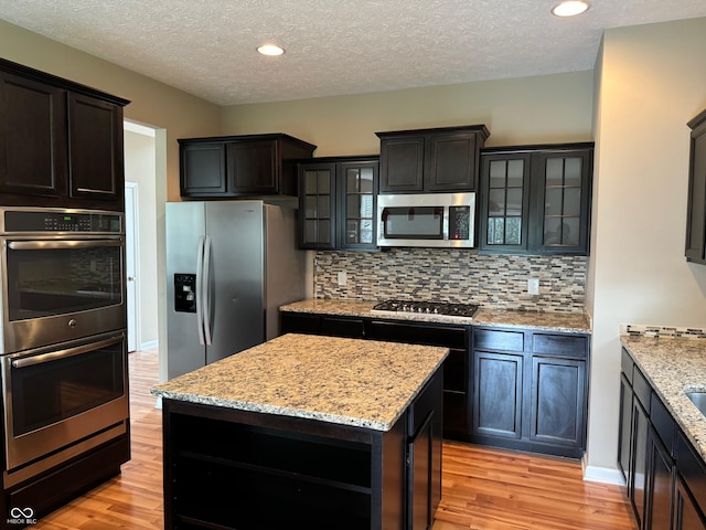 kitchen featuring light wood-type flooring, a textured ceiling, a kitchen island, and stainless steel appliances