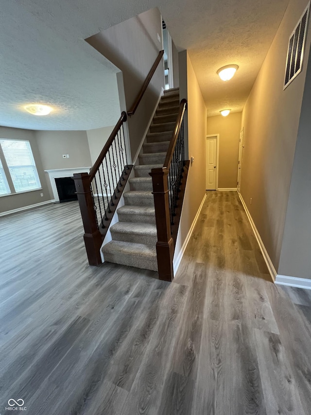 staircase featuring a textured ceiling, wood finished floors, visible vents, and baseboards