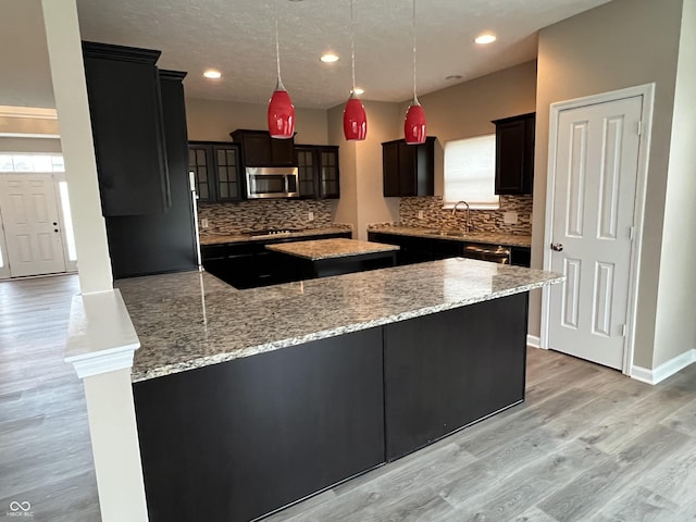 kitchen featuring glass insert cabinets, light stone counters, hanging light fixtures, stainless steel appliances, and light wood-style floors