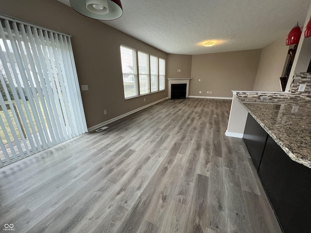 unfurnished living room with a fireplace, visible vents, a textured ceiling, wood finished floors, and baseboards