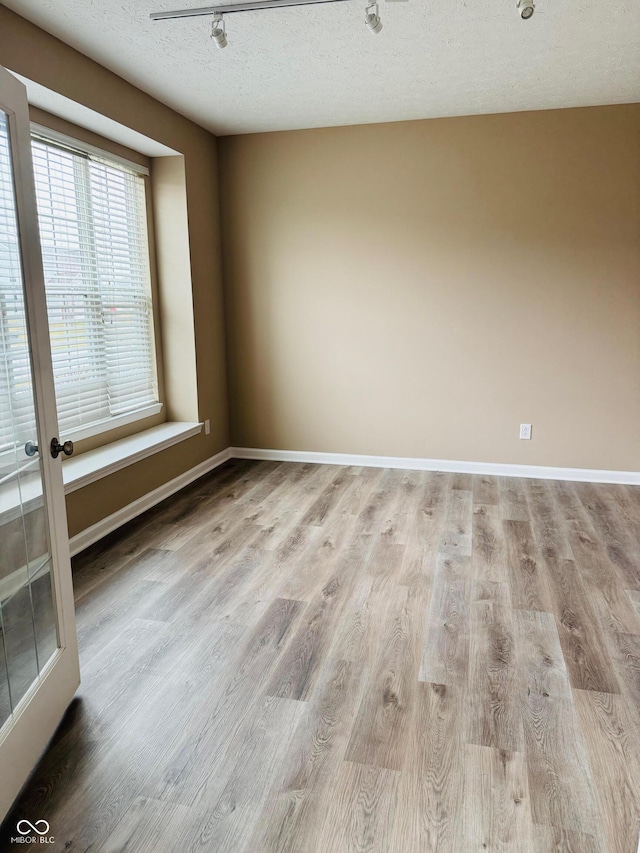 unfurnished room featuring baseboards, light wood-style flooring, and a textured ceiling