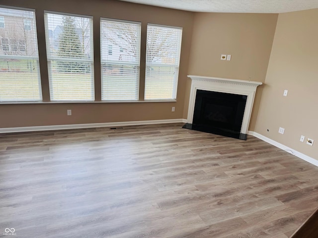 unfurnished living room with a fireplace with raised hearth, a textured ceiling, visible vents, baseboards, and light wood-style floors