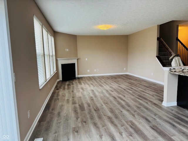 unfurnished living room with light wood-style floors, a fireplace with raised hearth, and baseboards