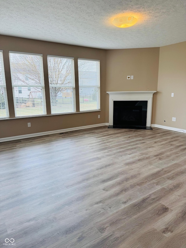 unfurnished living room with a fireplace with raised hearth, light wood-type flooring, a textured ceiling, and plenty of natural light