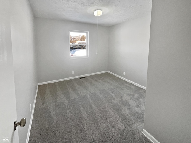 spare room with a textured ceiling and dark colored carpet