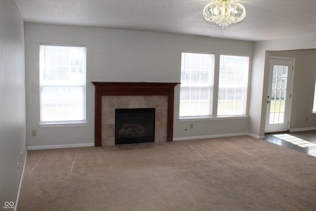 unfurnished living room featuring light carpet, an inviting chandelier, a textured ceiling, and a tile fireplace