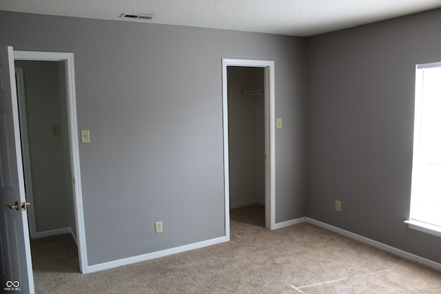 unfurnished bedroom featuring light colored carpet, a textured ceiling, a walk in closet, and a closet