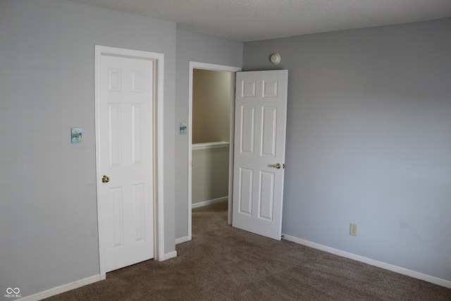 unfurnished bedroom with a textured ceiling and dark carpet