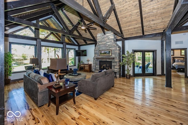 living room with plenty of natural light, hardwood / wood-style flooring, high vaulted ceiling, a stone fireplace, and ceiling fan