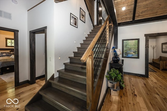 staircase featuring wood-type flooring, a towering ceiling, and wooden ceiling