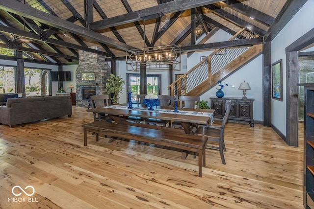 dining room with beamed ceiling, a stone fireplace, a chandelier, high vaulted ceiling, and hardwood / wood-style flooring