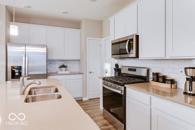 kitchen with pendant lighting, white cabinets, light hardwood / wood-style flooring, stainless steel appliances, and backsplash