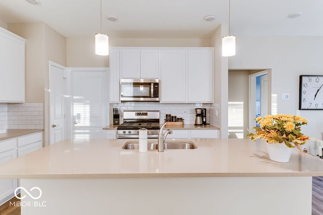 kitchen with an island with sink, wood-type flooring, stainless steel appliances, and decorative light fixtures