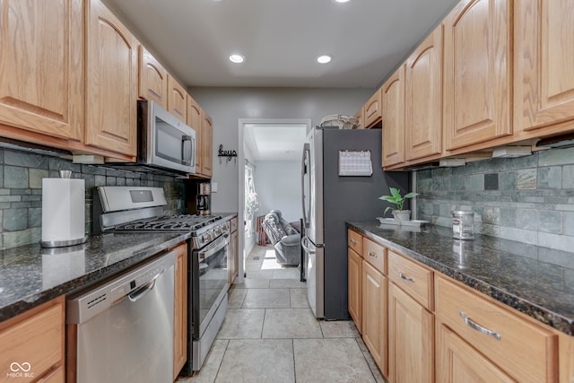 kitchen with appliances with stainless steel finishes, backsplash, dark stone countertops, and light brown cabinets