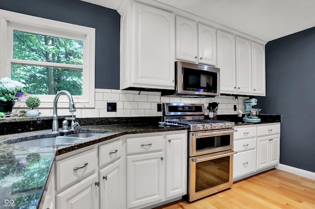 kitchen with decorative backsplash, white cabinetry, stainless steel appliances, light wood-type flooring, and sink