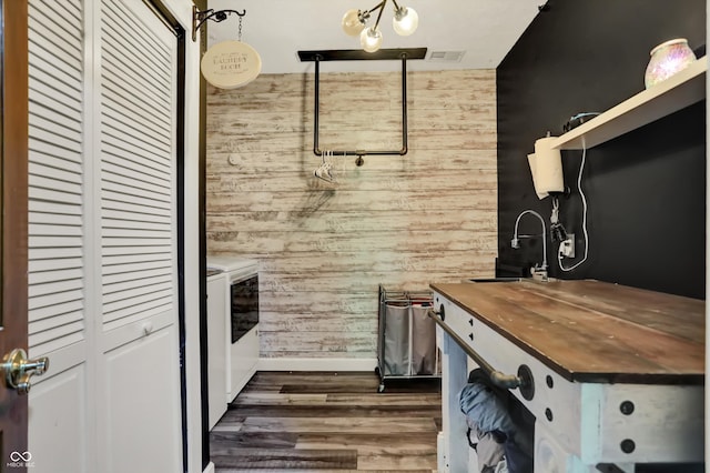 interior space featuring pendant lighting, washing machine and clothes dryer, wooden walls, dark hardwood / wood-style floors, and wood counters