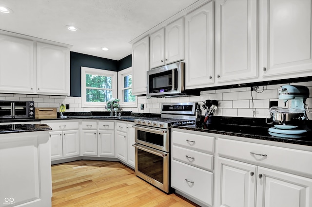 kitchen featuring appliances with stainless steel finishes, backsplash, light hardwood / wood-style floors, and white cabinetry