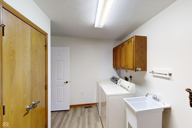 laundry area with sink, light wood-type flooring, cabinets, washing machine and dryer, and a textured ceiling