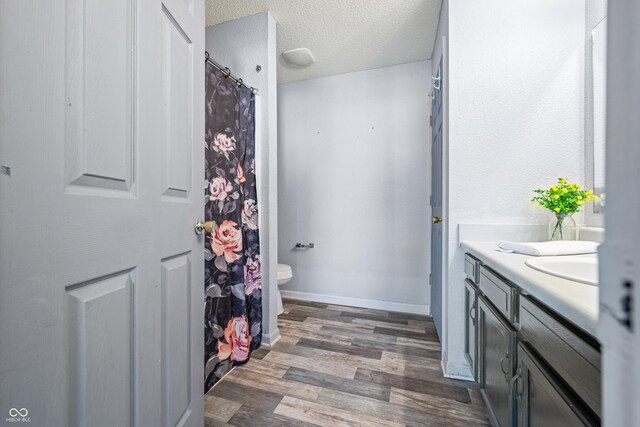 bathroom with a textured ceiling, wood-type flooring, vanity, and toilet