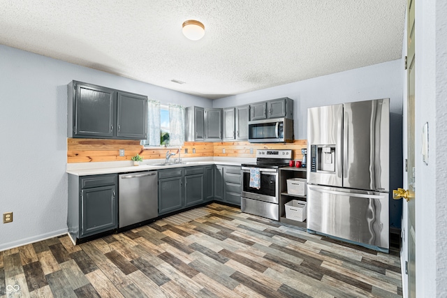 kitchen featuring gray cabinetry, dark wood-type flooring, decorative backsplash, appliances with stainless steel finishes, and a textured ceiling