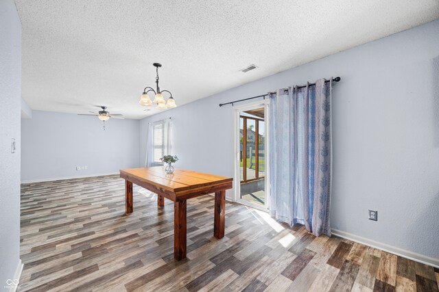 unfurnished dining area featuring ceiling fan with notable chandelier, dark hardwood / wood-style flooring, and a textured ceiling