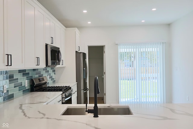 kitchen with appliances with stainless steel finishes, light stone countertops, sink, and white cabinets