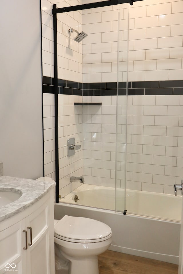 full bathroom with toilet, vanity, hardwood / wood-style floors, and bath / shower combo with glass door