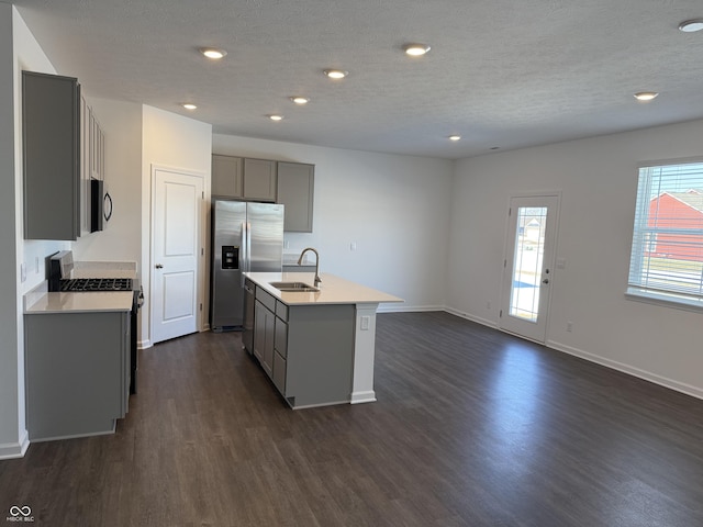 kitchen featuring sink, dark wood-type flooring, gray cabinets, appliances with stainless steel finishes, and a center island with sink