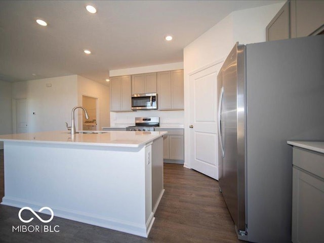 kitchen with dark wood-type flooring, sink, appliances with stainless steel finishes, gray cabinets, and a kitchen island with sink