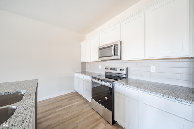 kitchen with decorative backsplash, light stone countertops, stainless steel appliances, light hardwood / wood-style flooring, and white cabinets