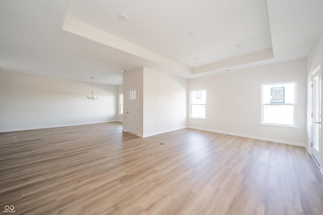 spare room featuring a chandelier, a raised ceiling, light hardwood / wood-style flooring, and a healthy amount of sunlight