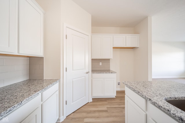 kitchen featuring tasteful backsplash, light hardwood / wood-style flooring, white cabinetry, and light stone counters