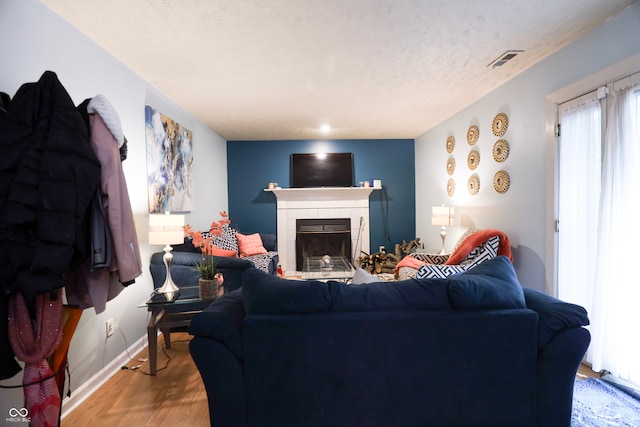 living room with a textured ceiling, a tiled fireplace, and hardwood / wood-style flooring