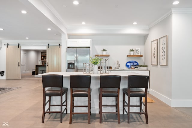 kitchen featuring sink, stainless steel refrigerator with ice dispenser, a breakfast bar, crown molding, and a barn door