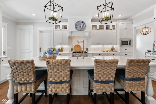 kitchen featuring a notable chandelier, a center island with sink, stainless steel microwave, and dark wood-type flooring