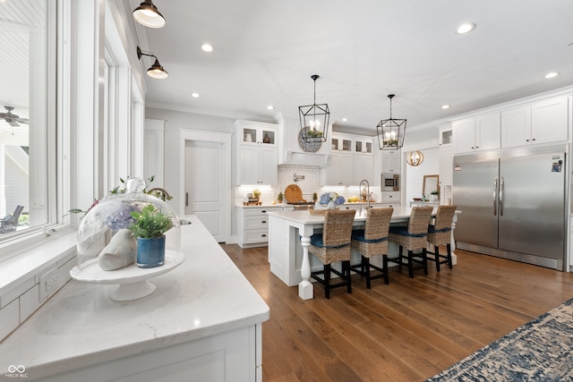 kitchen with white cabinets, built in appliances, dark wood-type flooring, and a large island