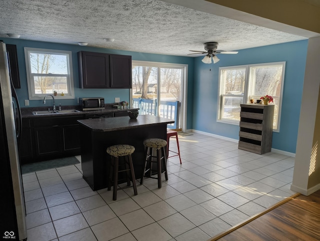 kitchen with a kitchen island, sink, stainless steel fridge, a kitchen breakfast bar, and light tile patterned floors