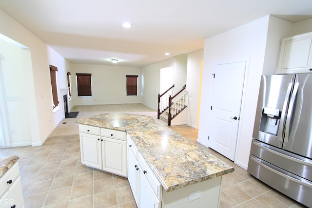 kitchen featuring a kitchen island, white cabinetry, stainless steel fridge, light tile patterned floors, and light stone countertops