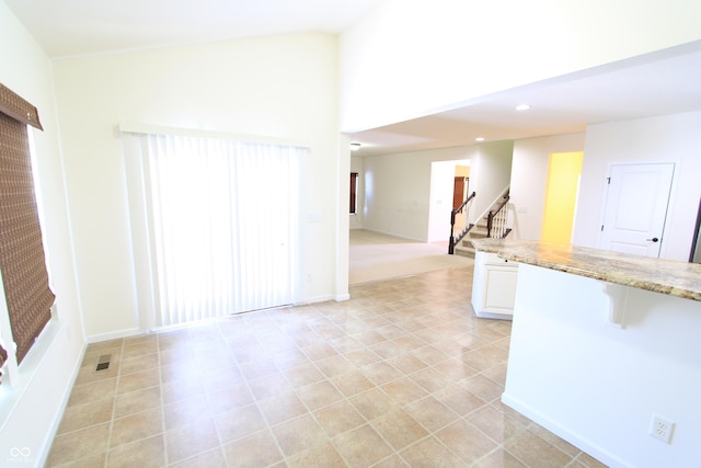 kitchen with a towering ceiling, light tile patterned floors, white cabinets, and light stone counters