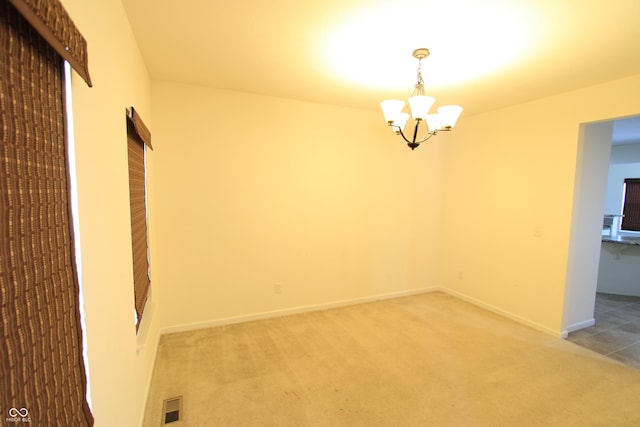 carpeted empty room featuring a notable chandelier