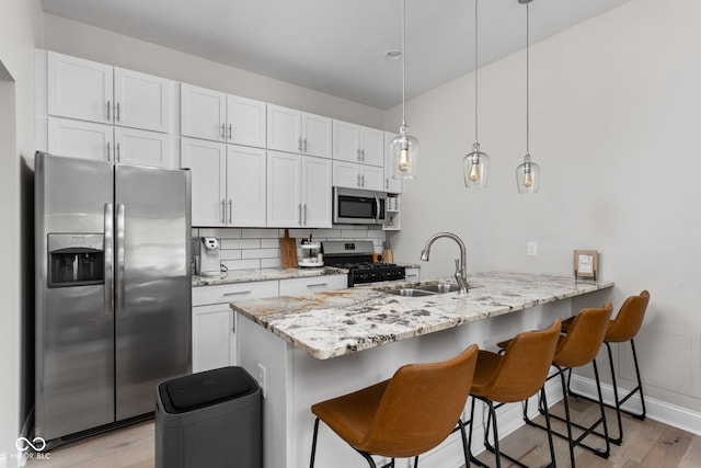 kitchen featuring sink, white cabinets, kitchen peninsula, hanging light fixtures, and appliances with stainless steel finishes