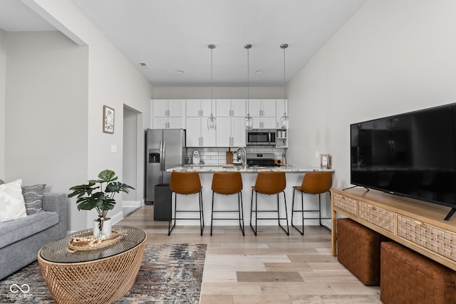 kitchen with light wood-type flooring, light stone counters, white cabinetry, stainless steel appliances, and backsplash