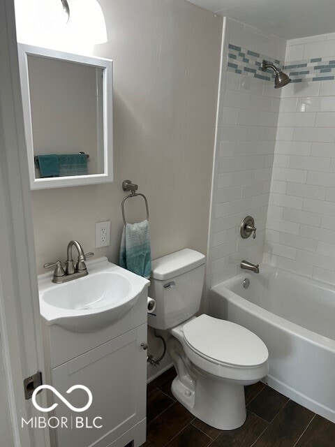 full bathroom featuring hardwood / wood-style floors, tiled shower / bath combo, vanity, and toilet