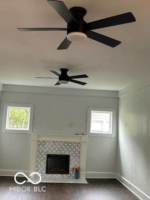 unfurnished living room featuring ceiling fan, a fireplace, a wealth of natural light, and dark hardwood / wood-style flooring