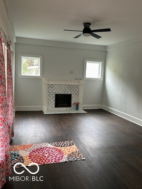 unfurnished living room with dark wood-type flooring, plenty of natural light, ceiling fan, and a tile fireplace