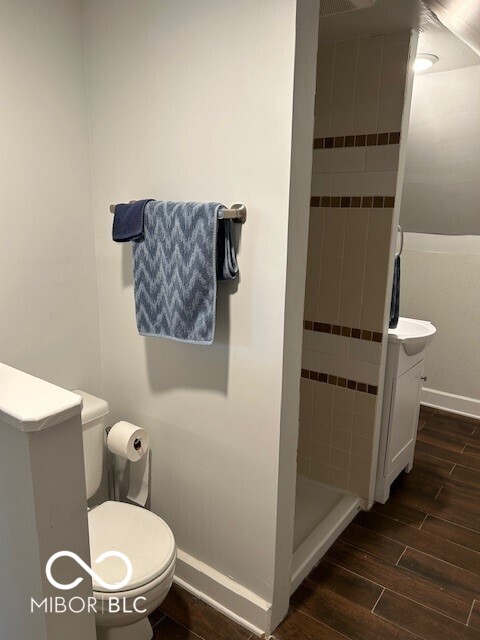 bathroom featuring a tile shower, hardwood / wood-style flooring, vanity, and toilet