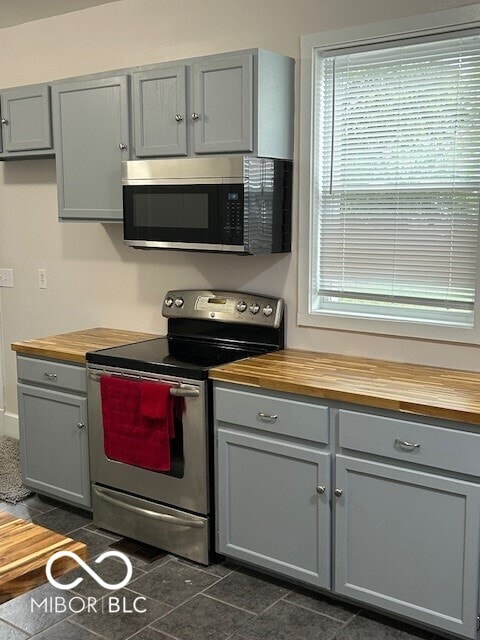 kitchen featuring gray cabinetry, stainless steel appliances, dark tile patterned floors, and wood counters