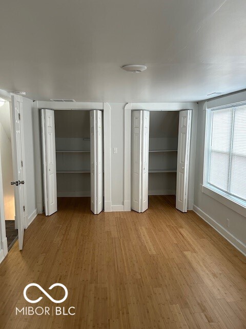 unfurnished bedroom with wood-type flooring and two closets